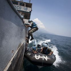 Mitarbeiter der UN mit blauen Helmen steigen von einem Schlauchboot auf ein größeres Schiff um.