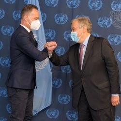 UN-Generalsekretär António Guterres (rechts) begrüßt Außenminister Heiko Maas. Zwei Männer in Anzug und mit Mund-Nasen-Schutz begrüßen sich vor einem UN-Banner per Ellenbogenberührung.