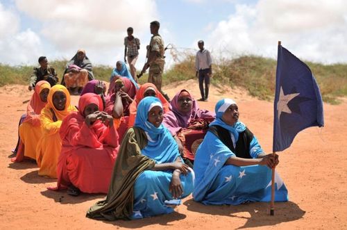 Eine Gruppe von Mädchen sitzt auf sandigem Boden. Ein Mädchen hält die somalische Flagge.