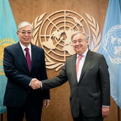 UN-Generalsekretär António Guterres (links) trifft Kasachstans Präsident Kassym-Schomart Tokajew Zwei Männer schütteln sich die Hand, im Hintergrund sieht man das Logo der Vereinten Nationen, die blaue UN-Flagge und die Flagge Kasachstans.