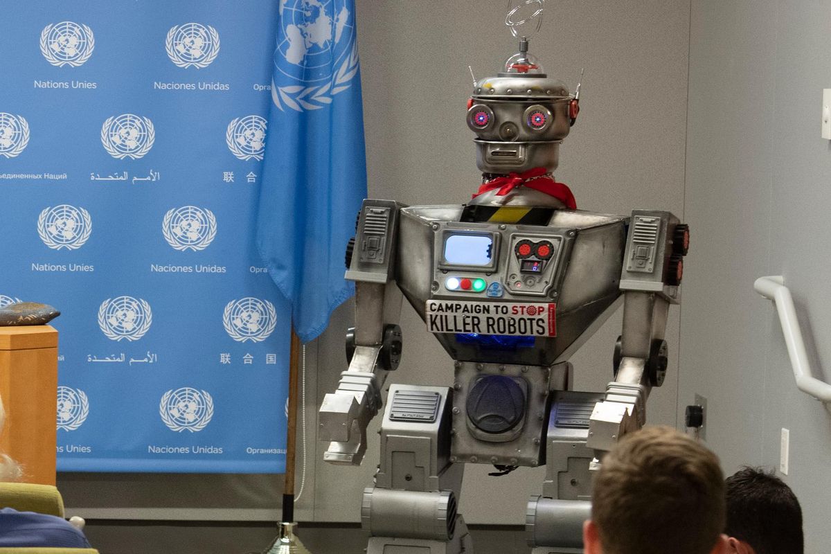 Vor einem Banner mit UN-Logo steht ein Roboter. An seiner Brust haftet ein Schild mit der Aufschrift: Stop Killer Robots