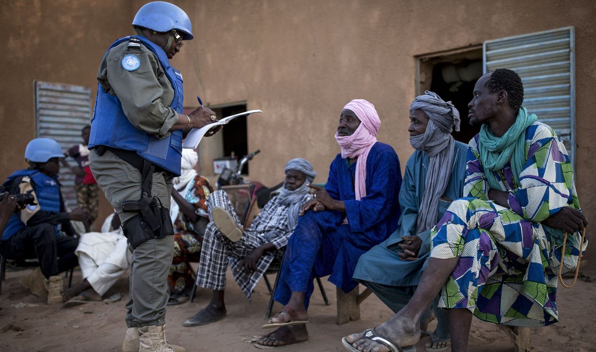 Ein Soldat steht vor drei sitzenden afrikanischen Männern.