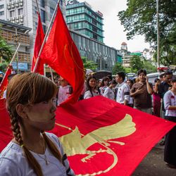 Teilnehmende anlässlich einer jährlichen Gedenkveranstaltung in Yangon Eine Frau steht vor einigen rot-gelben Fahnen inmitten einer Demonstration