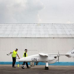 Zwei Techniker der UN stehen vor einem Hangar und bereiten eine Drohne zum Start vor.