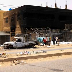 Eine Straße mit zerbombten Autos und Gebäuden im Hintergrund in Sudan.