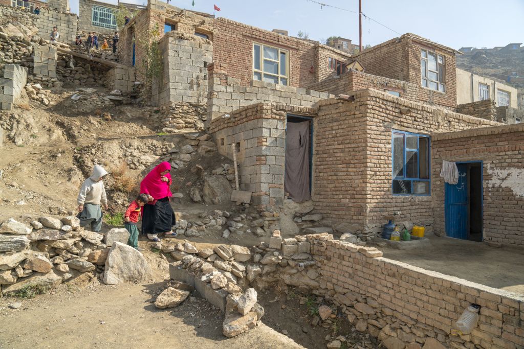 Eine afghanische Frau und ihre zwei Kinder laufen einen kleinen Weg hinunter zu ihrer notdürftigen Behausung.